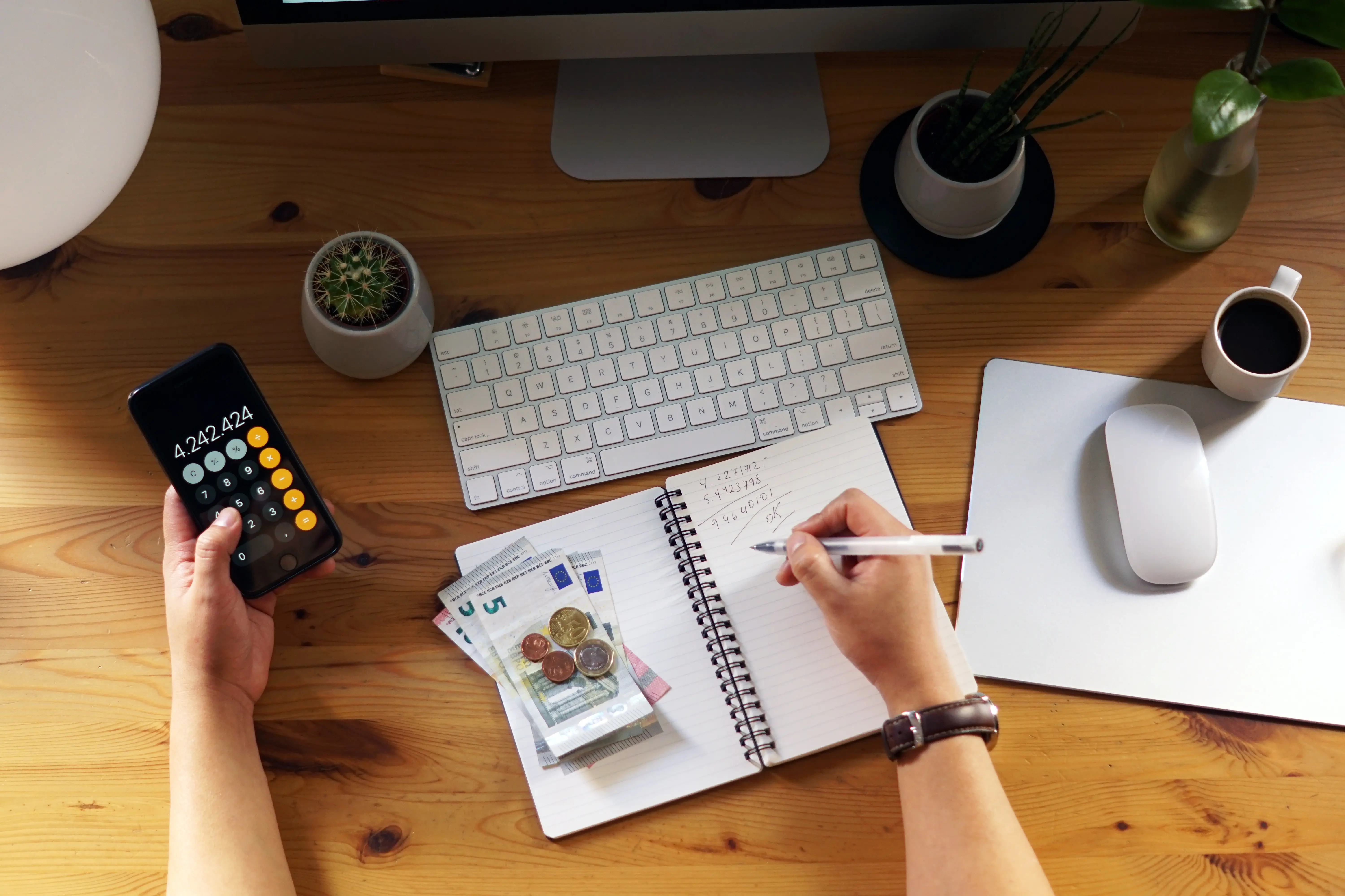 Person managing money and writing in notebook with phone calculator and euro bills — personal finance planning setup