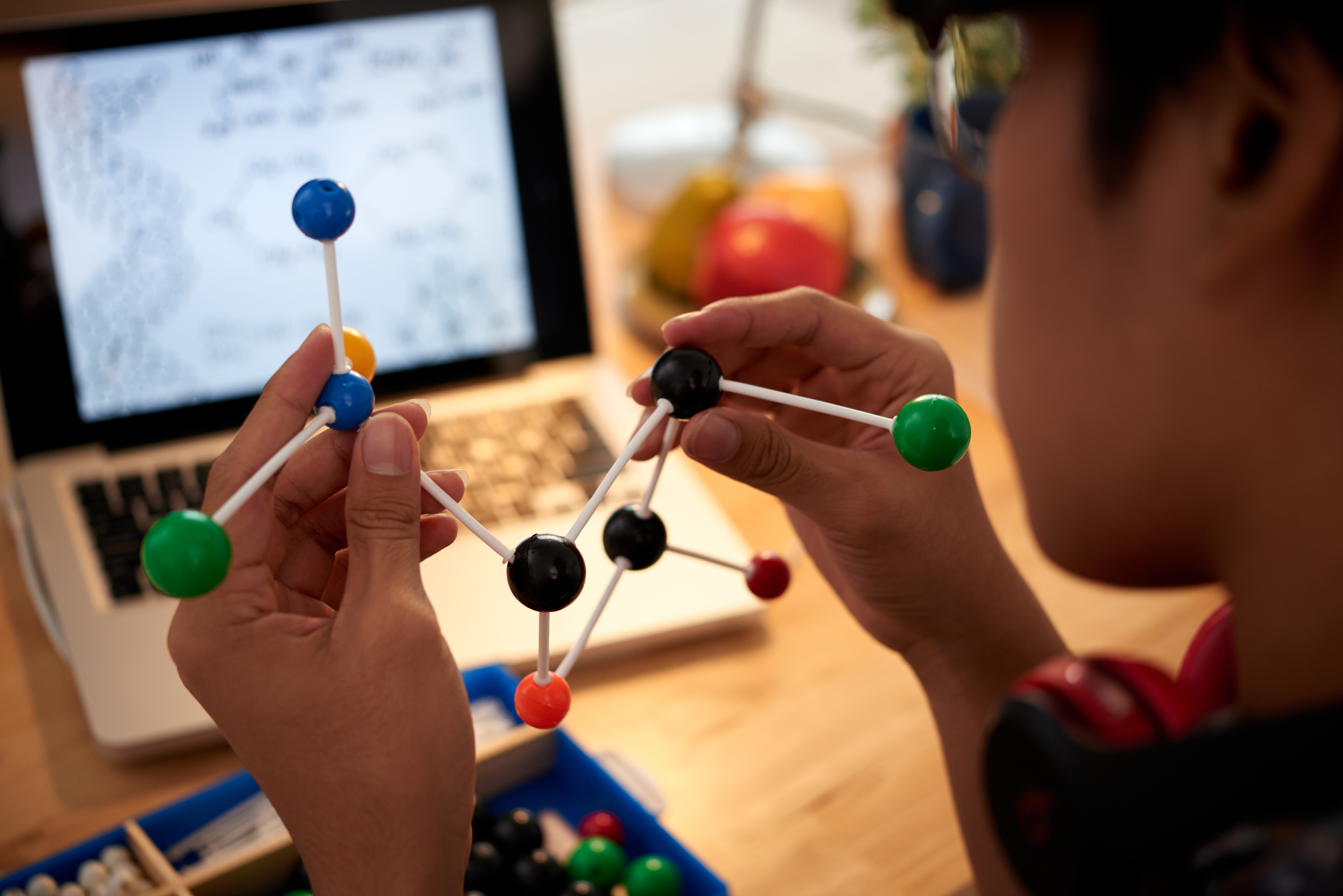 A person studying molecular structures using a model and a laptop, representing the gamification of cognitive development and learning.
