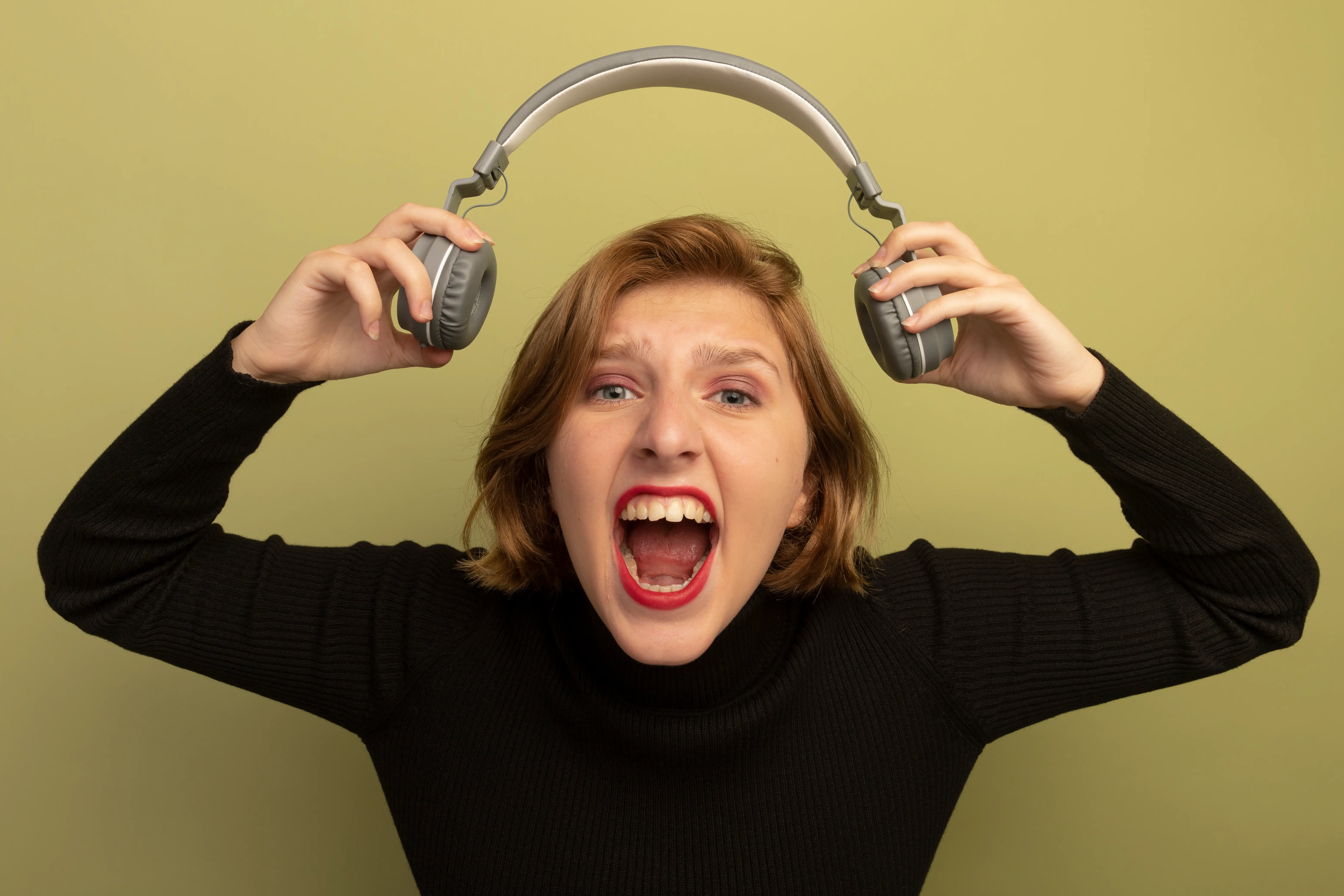 Frustrated woman screaming while holding headphones — overwhelmed by constant background noise