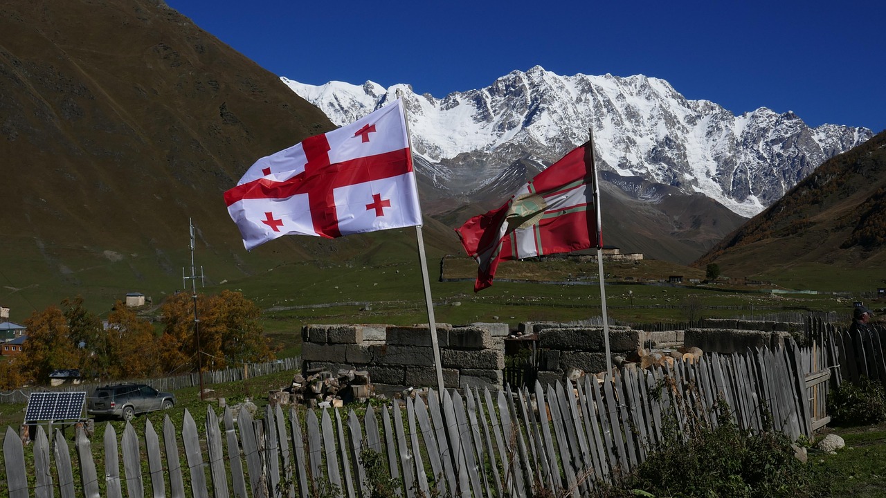 Georgian and Svan flags flying in a remote mountain village in Svaneti, Georgia with snow-covered Caucasus Mountains in the background