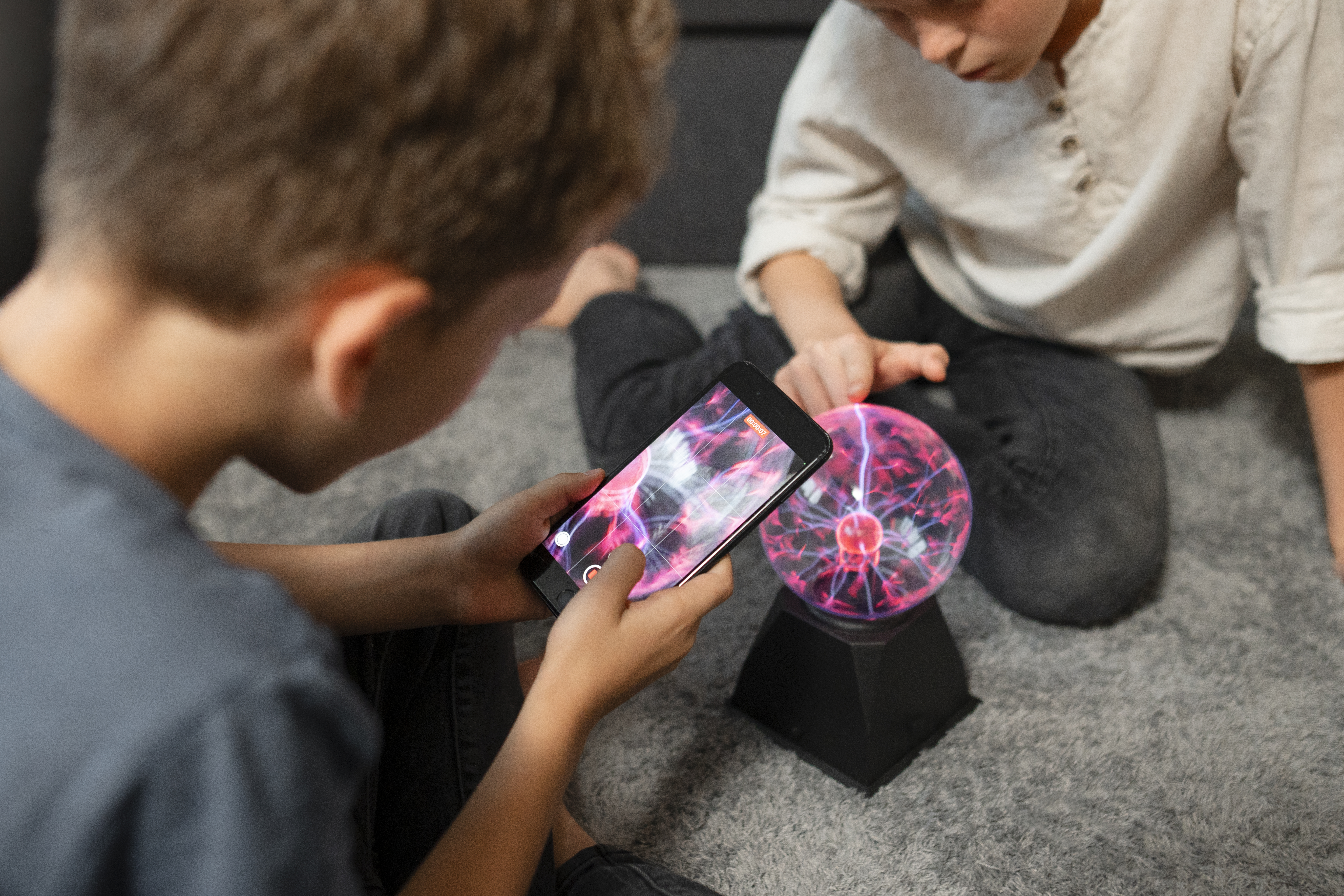 Two children experimenting with a plasma ball and smartphone, exploring technology's impact on cognitive development.