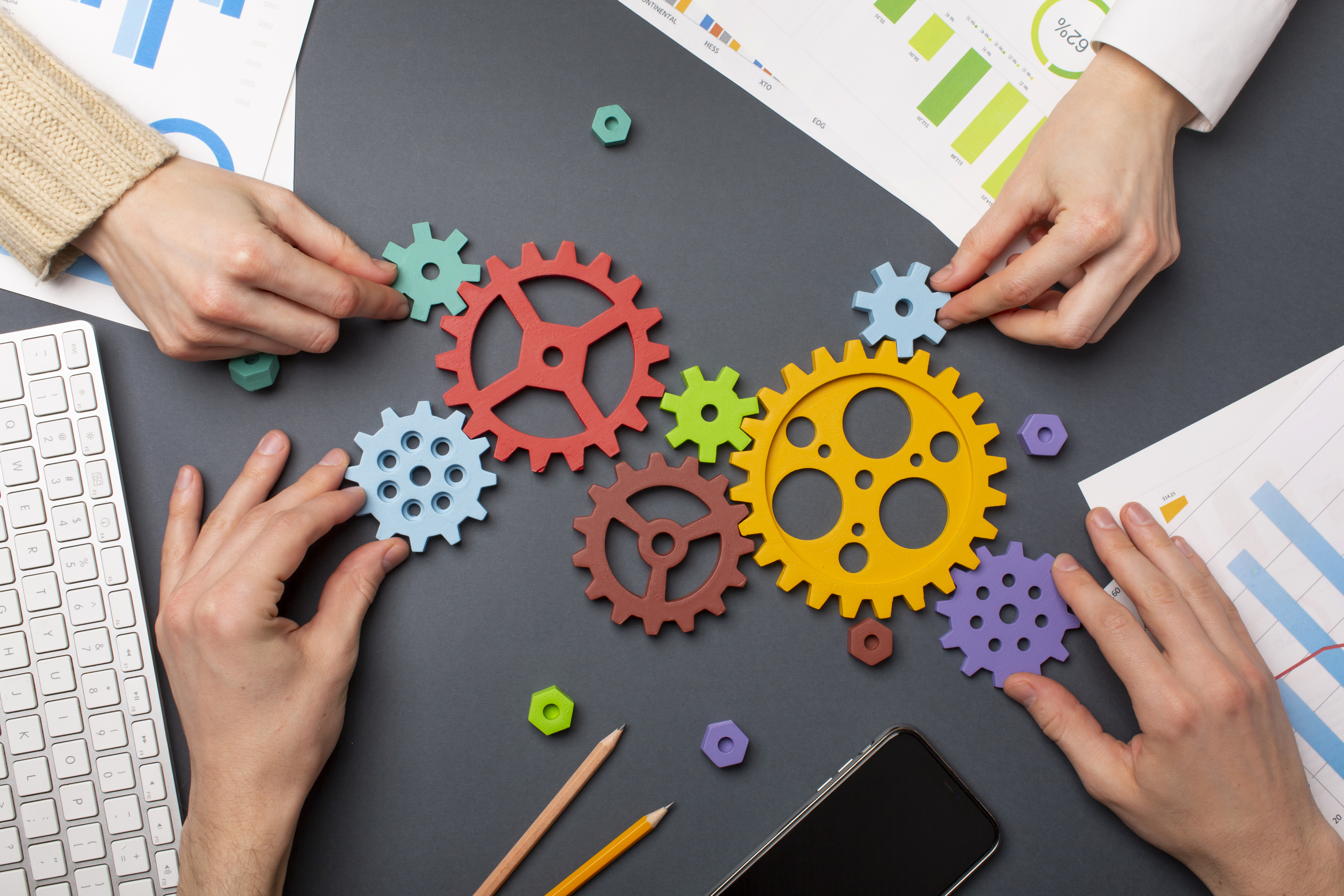 Colorful gears being arranged on a table, symbolizing teamwork and collaboration, with charts and a smartphone nearby.