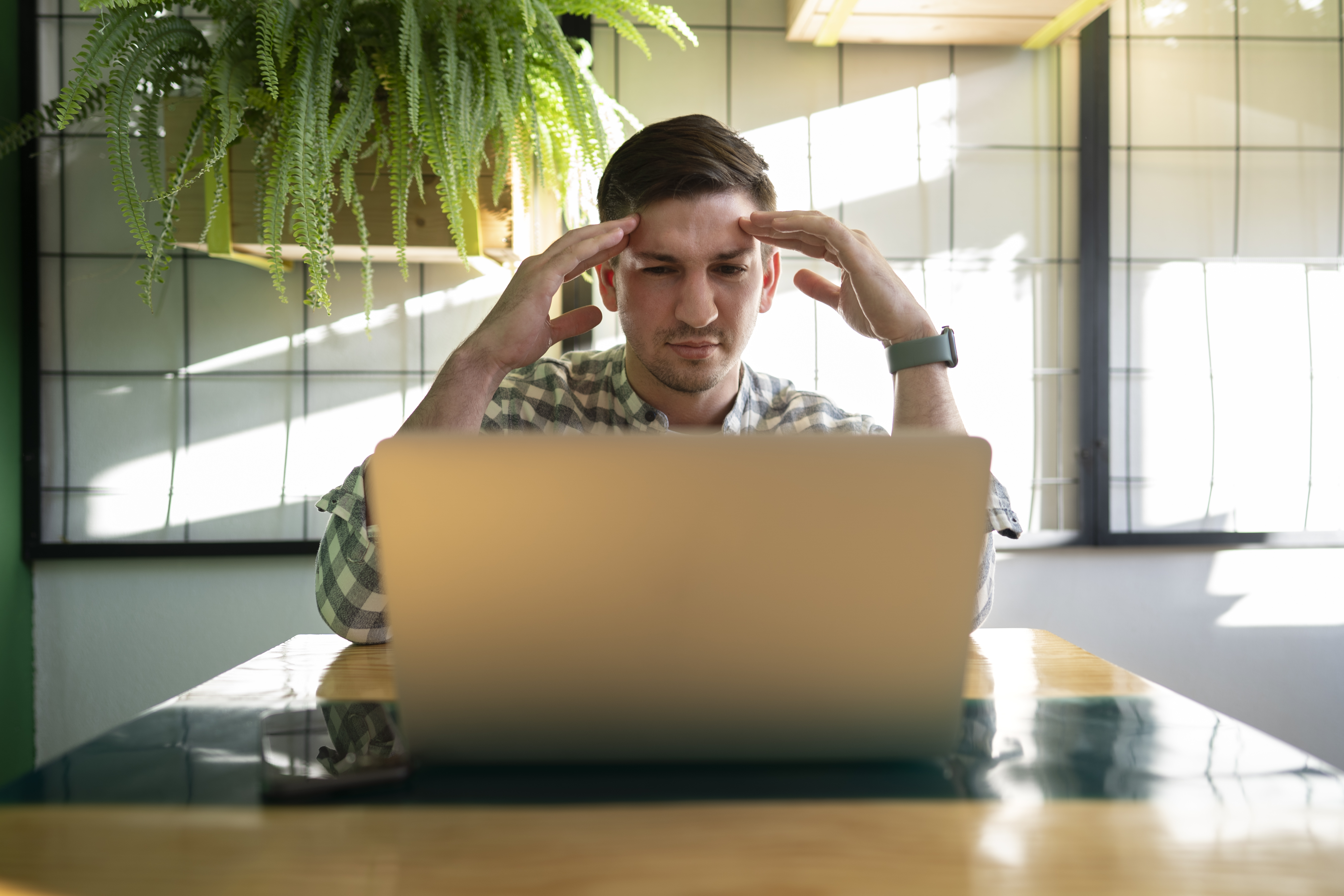 Man sitting at laptop with hands on temples, experiencing mental fatigue and difficulty focusing due to content overload